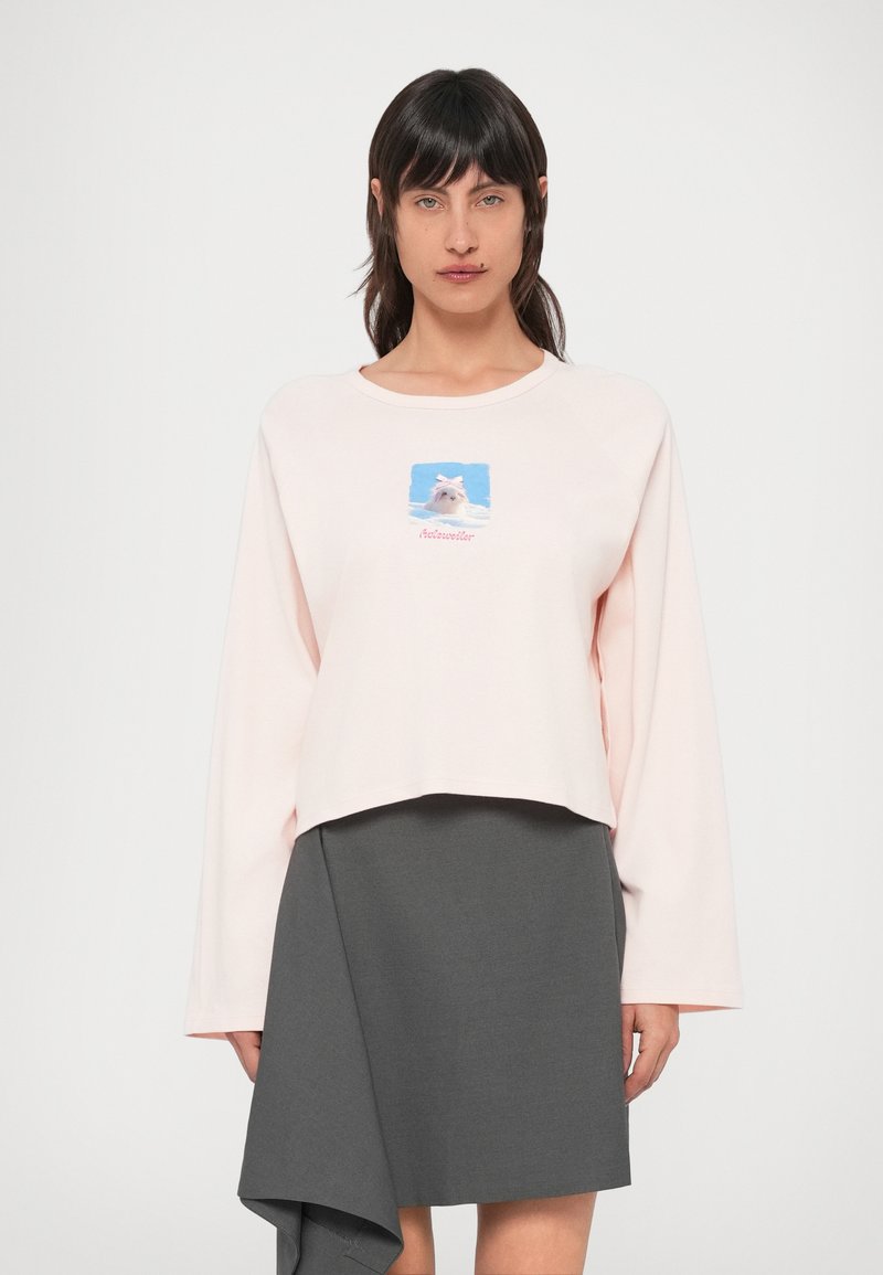 Hele roosa lühendatud dressipusa pikkade varrukatega, millel on koera graafika sinisel taustal koos lipsuga, kombineeritud tumehallide asümmeetrilise seelikuga.