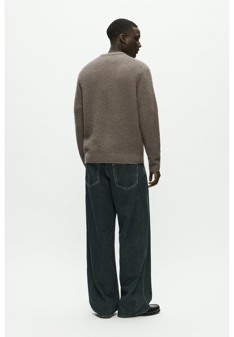 Pull en maille texturé gris avec un col rond, associé à un jean large bleu foncé. La tenue présente une coupe décontractée et un design minimaliste.