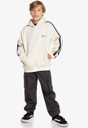 Crème hoodie met een voorkantzak, zwart-wit gestreepte mouwen, met een blauw berglogo; gecombineerd met donkere cargobroeken.