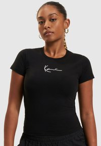 Black fitted t-shirt made of cotton, featuring a white graphic design at the chest. Short sleeves and a round neckline.