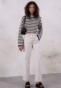Sweater riscado em preto e branco, corte descontraído, combinado com jeans de cintura alta off-white, bolsa preta e sandálias pretas, contra um fundo texturizado.