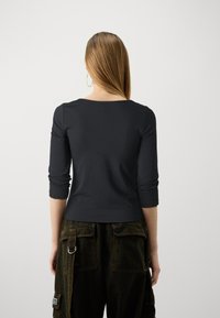 Black fitted long-sleeve top with a round neckline, paired with dark green cargo pants featuring side pockets and metal accents.