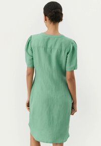 Grünes Leinenkleid mit kurzen Puffärmeln, rundem Ausschnitt und gerader Silhouette, mit einem leicht längeren Rückensaum.