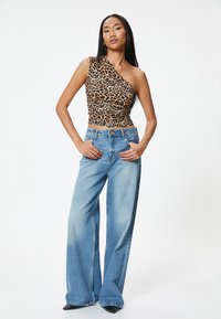 Top asimétrico de estampado de leopardo, hecho de tejido elástico, combinado con jeans de pierna ancha en azul claro, con un lavado desvanecido y un cierre de botón clásico.