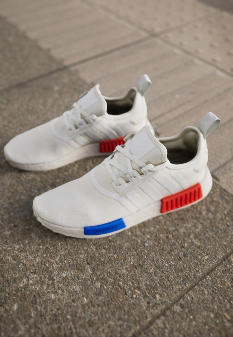 Weiße Sportschuhe aus strukturiertem Material, mit blauen und roten Akzenten an der Sohle und drei weißen Streifen an der Seite.
