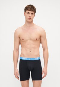 Juodi šortai bokseriai su mėlynu Nike juosmeniu, pagaminti iš tamprių audinių, pasižymintys prigludusia forma ir vidutinio ilgio dizainu.
