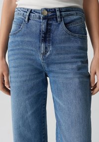 Lichtblauwe denim jeans met een hoge taille, voorzien van voorzakken, een ritsenopening en een metalen knoopsluiting. Soepele textuur en ontspannen pasvorm.