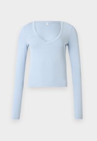 Ανοιχτό μπλε crop top με μακριά μανίκια και V-λαιμόκοψη, με απλή υφή, παρουσιάζεται σε ουδέτερο ανοιχτό γκρι φόντο.