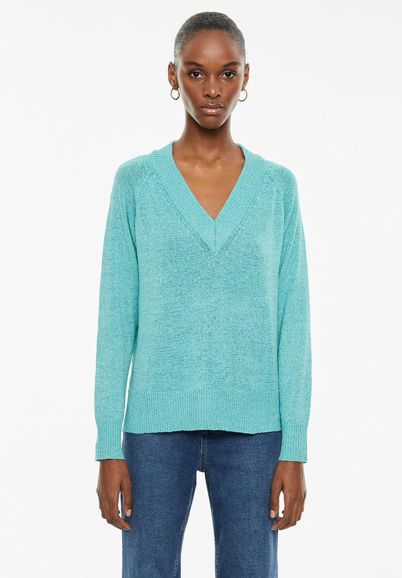Light turquoise sweater with a v-neck, long sleeves, and ribbed hem. Made from soft material with a textured finish.