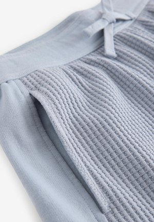 Vêtement de couleur bleu clair doté d'un tissu texturé et côtelé avec des accents lisses. Comprend un détail à nouer à la taille pour un ajustement.