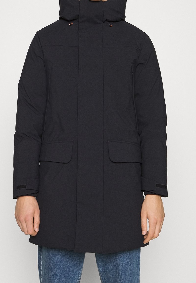 Zwarte parka met capuchon gemaakt van waterafstotend materiaal, voorzien van twee voorzakken, verstelbare manchetten en een recht ontwerp.