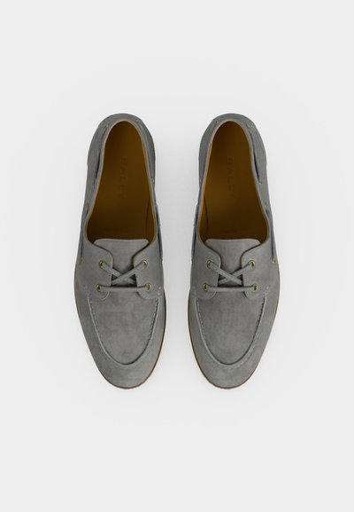 Γκρι σουέντ παπούτσια τύπου boat με δερμάτινα κορδόνια και στρογγυλεμένη μύτη, φωτογραφημένα από πάνω σε λευκό φόντο.