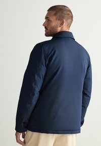 Navy blue padded jacket with a collar, featuring a smooth texture and simple design. Includes visible stitching and cuff details.