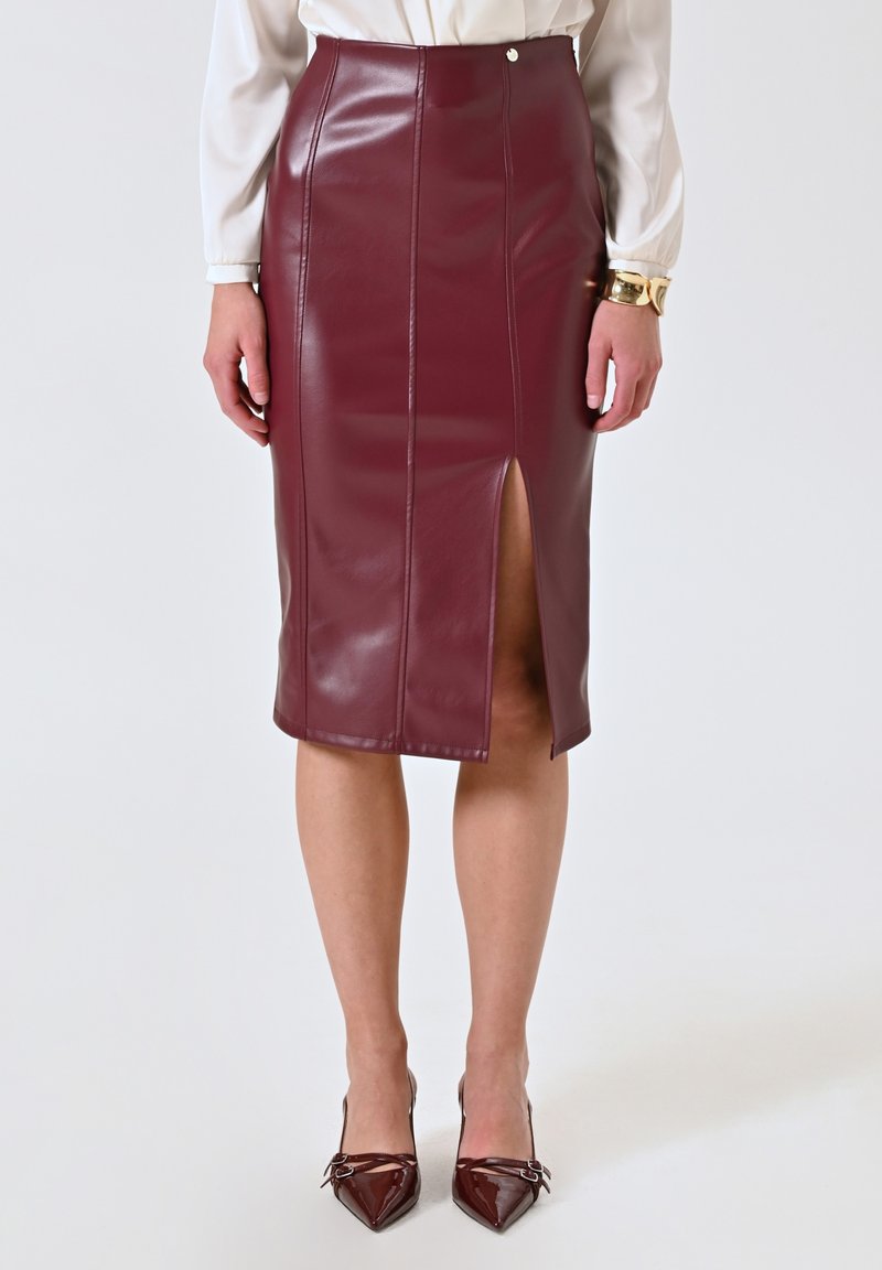 Jupe crayon bordeaux, longueur genoux, en faux cuir brillant avec fente sur le devant, détails cousus et bouton décoratif sur la taille.