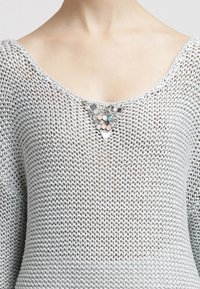 Maglione grigio chiaro a maglia con scollatura ampia. Presenta decorazioni di gioielli in tonalità pastello e metalliche sulla scollatura, aggiungendo texture.