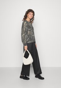 Blusa preta de manga longa com um padrão ondulado e neutro; combinada com calças largas pretas e uma pequena bolsa branca. Sapatos pretos completam o visual.