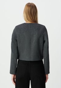 Krótką, ciemnoszaro wełnianą kurtkę o mieszanym składzie z wyraźnie zarysowanymi ramionami i długimi rękawami, z prostym szwem na plecach i bez widocznych zapięć.