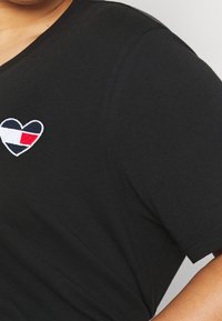 Sort bomulds T-shirt med et hjerteformet broderet logo i navy, hvid og rød på venstre for. Korte ærmer og rund halsudskæring.