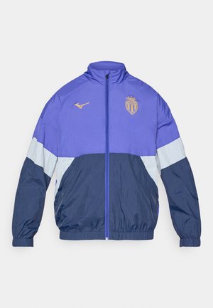 Lila in mornarica vetrovka z zadrgo spredaj, elastičnimi manšetami in svetlo modrimi detajli. Ima logotip na prsih. Lahka material.