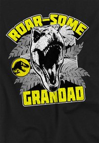 Black t-shirt featuring a graphic of a roaring dinosaur, surrounded by green leaves, with the text "ROAR-SOME GRANDAD" in yellow.