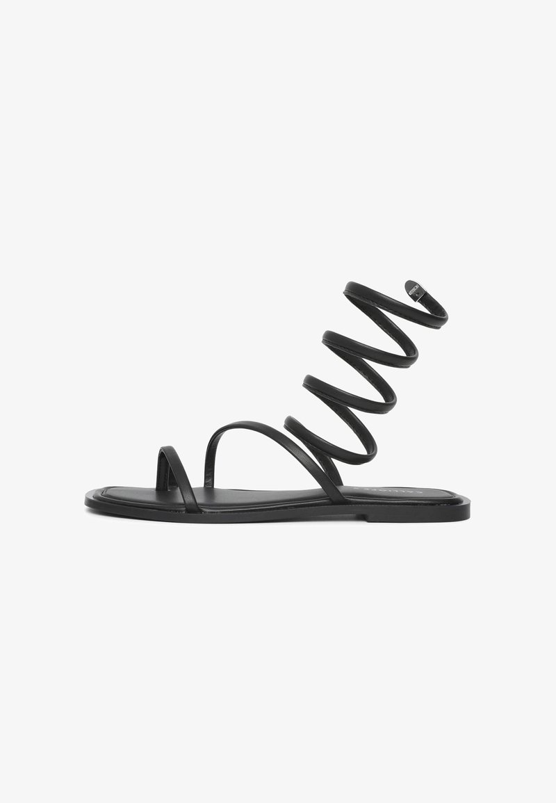 Schwarze Sandale mit flacher Sohle, dünnen Riemen und einem spiralförmigen Design, das nach oben verläuft. Hergestellt aus glattem Material und mit minimalistischen Akzenten.