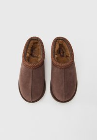 Pair of brown suede UGG slippers with plush fur lining and decorative stitching around the opening on white background.