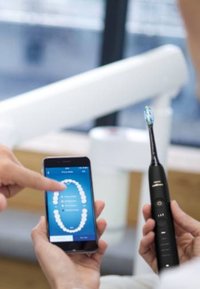 Spazzolino elettrico nero con testa a setole blu tenuto in una mano, abbinato a uno smartphone che mostra un'app dentale.