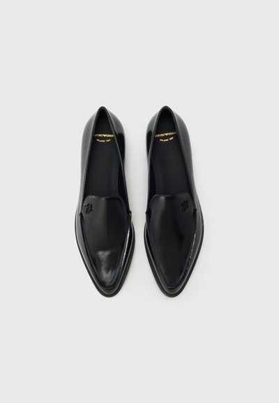 Μαύρα δερμάτινα παπούτσια χωρίς κορδόνια με σχεδιασμό μυτερού τοξεύματος. Ομαλή υφή με διακριτική ανάγλυφη λεπτομέρεια λογότυπου στο πάνω μέρος.