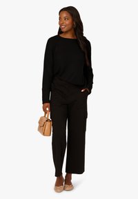 Černý žebrovaný svetr s širokým výstřihem, společně s černými cargo kalhotami s náprsními kapsami. Světle hnědá kabelka a pletené boty dokončují vzhled.