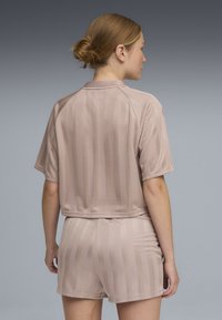 Γυναίκα με ανοιχτό καφέ μαλλιά σε κότσο, που φοράει μπεζ τοπ με κοντά μανίκια και ταιριαστό σορτς με διακριτικές κάθετες ρίγες, με την πλάτη προς τα εμπρός.