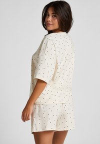 Crème katoenen loungewear set met zwarte stippen; bevat een top met korte mouwen en bijpassende shorts, losse pasvorm, zachte textuur en zijsplitten.