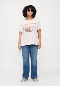 Light pink cotton t-shirt with "Coconut" graphic and coconuts illustration. Paired with blue denim wide-leg jeans and silver sneakers.