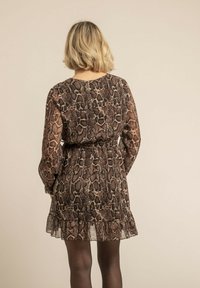 Robe courte et transparente marron avec un motif serpent, taille cintrée et ourlet froncé. Des manches longues légèrement bouffantes complètent le design.