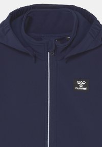 Marineblaue Kapuzenjacke aus glattem, dehnbarem Material, mit Frontreißverschluss und schwarzem Logo-Patch auf der linken Brust. Schlanke, taillierte Passform.