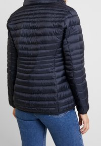 Veste en duvet navy avec un design matelassé, dotée d'un col haut, d'une texture douce et d'une silhouette ajustée. Convient par temps froid.