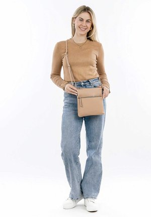 Beige crossbody bag made of smooth leather, featuring a front zip pocket, minimalistic design, and adjustable strap. Paired with casual jeans.