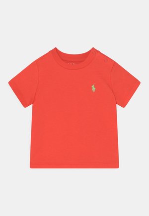 Czerwona koszulka niemowlęca z krótkim rękawem, z zielonym logo zawodnika polo na piersi oraz zatrzaskami na lewym ramieniu.