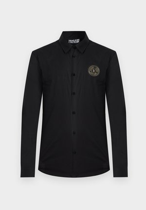 Musta pitkähihainen napillinen kauluspaita, jossa on kaulus ja Versace Jeans Couture -logopläkki vasemmassa rinnassa.