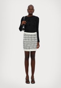 Black long-sleeve top with butterfly pattern, white and black tweed mini skirt with knit trim, and strappy black high-heeled sandals.