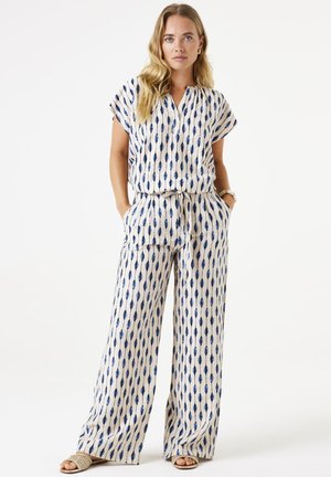 Bedrukt tweedelig outfit met een crèmekleurige basis en een marineblauw, bladvormig patroon. Heeft korte mouwen, een gestrikte taille en brede broekspijpen.