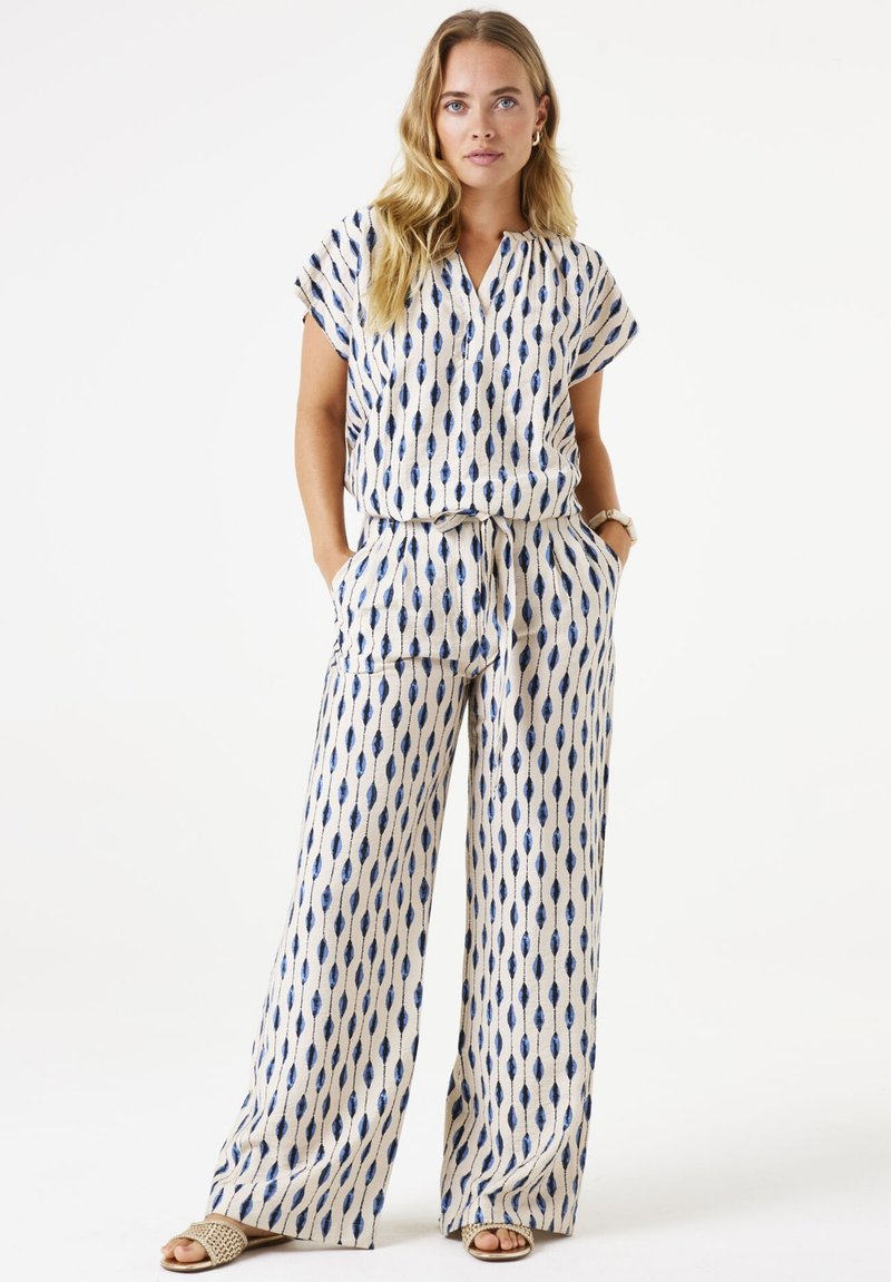 Bedrukt tweedelig outfit met een crèmekleurige basis en een marineblauw, bladvormig patroon. Heeft korte mouwen, een gestrikte taille en brede broekspijpen.