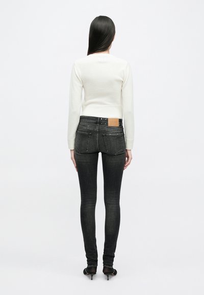 Λευκό κοντό πουλόβερ με ραμμένες μανσέτες, συνδυασμένο με σκούρες γ�κρι στενές τζιν που περιλαμβάνουν πίσω τσέπες και μια καφέ δερμάτινη ετικέτα στη ζώνη.