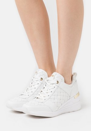 White leather sneakers with a quilted design, gold accents, flat laces, and a wedge heel. Smooth texture and rounded toe.