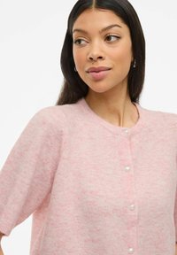 Cardigan rosa con maniche corte, realizzato in materiale morbido. Presenta un colletto rotondo e dettagli di bottoni simili a perle lungo il davanti.