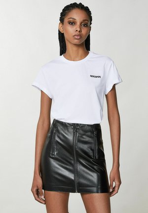 T-shirt in cotone bianco con maniche corte e logo "PATRIZIA PEPE" in nero. Abbinato a una mini gonna in pelle nera con tasche con zip.