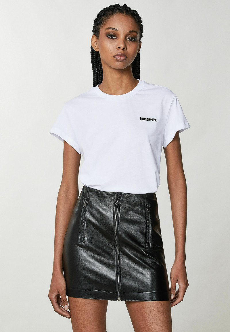 T-shirt in cotone bianco con maniche corte e logo "PATRIZIA PEPE" in nero. Abbinato a una mini gonna in pelle nera con tasche con zip.