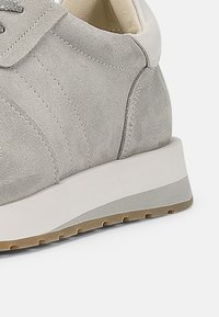 Grå semsket sneakers med hvit hælakkent. Har en tykk, teksturert såle med lett brun gummisåle. En enkel, stilren design.