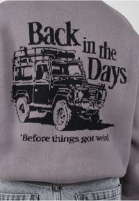Texte "Back in the Days" avec un véhicule tout-terrain vintage et "Before things got weird" au dos d'un pull gris tricoté.