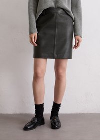 Zwarte leren rok met een rechte snit, voorzien van een voornaad detail. Gepaarde met een grijze gebreide trui en zwarte loafers met sokken.