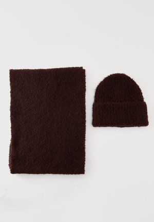 Écharpe en tricot texturé marron foncé et bonnet assorti posés à plat sur une surface blanche.